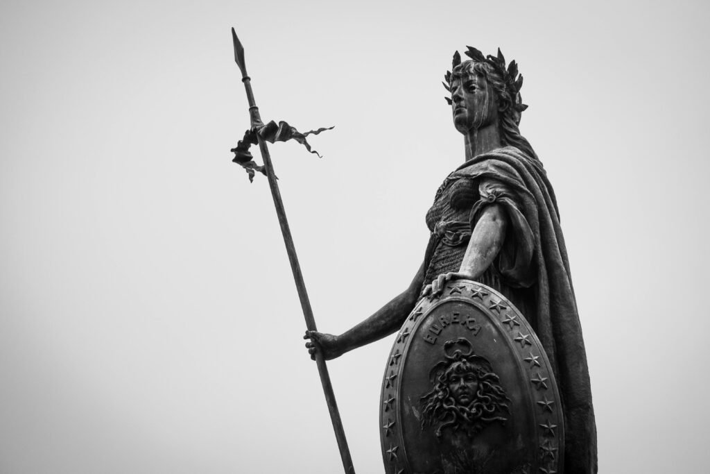A monochrome photograph showcasing a classic statue holding a spear and shield, exuding timeless strength.